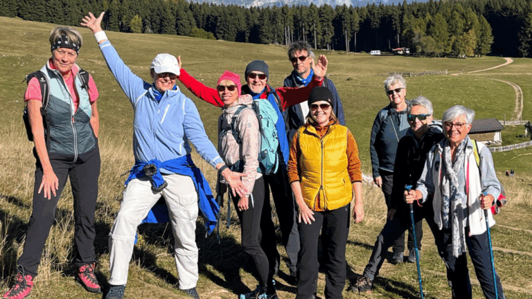 Gruppe von 9 Personen steht im leichten Anstieg vor Feldern und Hintergrund Wald. Zwei Personen, Frau und Mann, recken Arme in die Höhe. Die anderen blicken freundlich in die Kamera. Alle tragen Sportkleidung