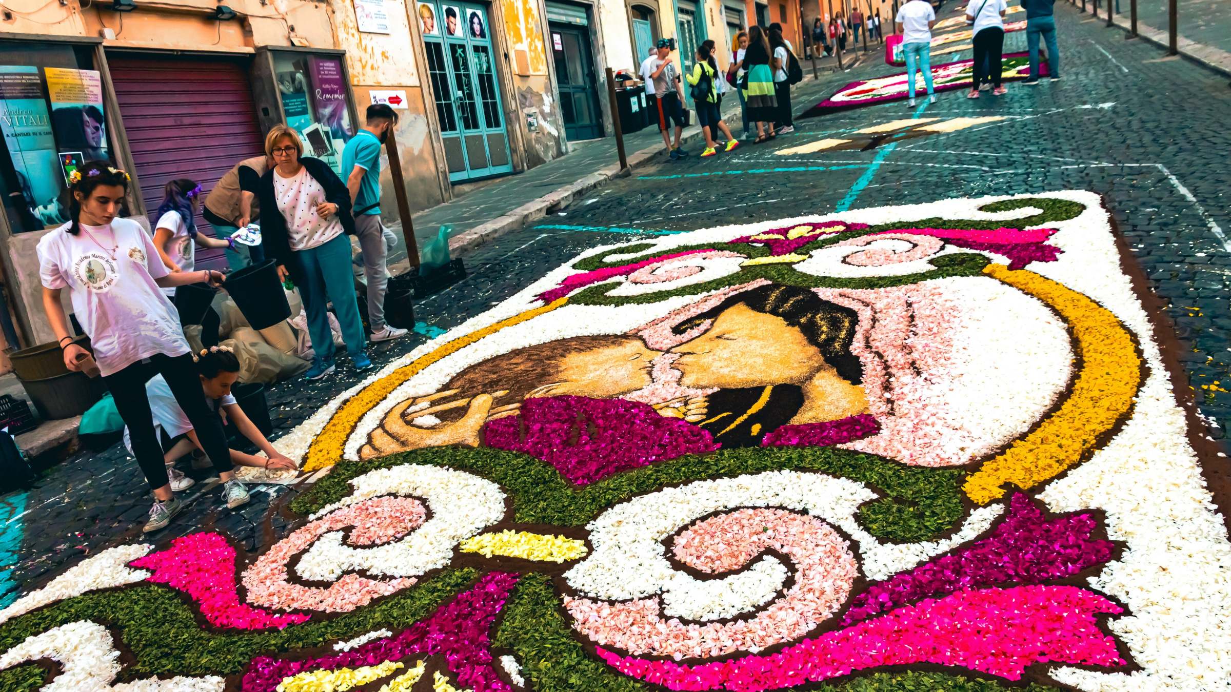 Infiorata in Spello: Menschen legen Blütenmuster in einer gepflasterten Gasse in Mittelitalien.
