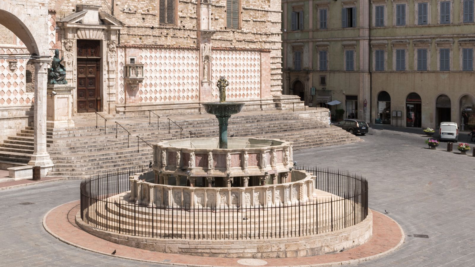 Blick auf den eingegitterten Brunnen von Perugia und die in Sandtönen gehaltene Kathedrale, typisch für Kirchen in Umbrien